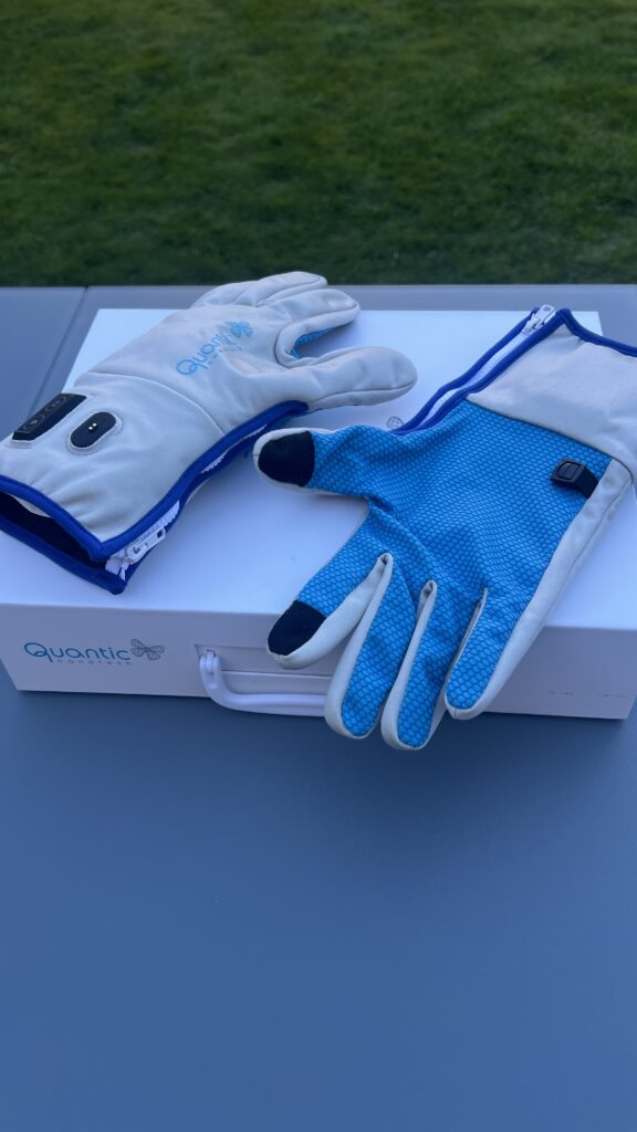 Un par de Guantes Electrónicos Q1 azul y blanco sobre una caja blanca con asa, en mesa exterior y césped, ideal para artrósis.